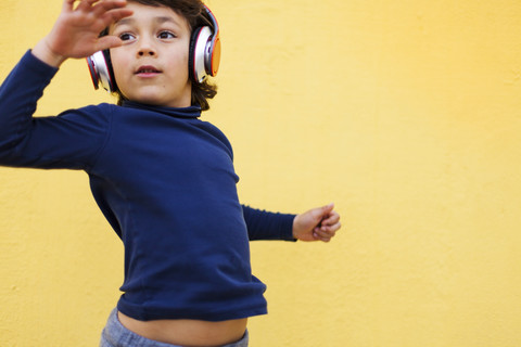 Tanzender kleiner Junge vor einer gelben Wand, der mit Kopfhörern Musik hört, lizenzfreies Stockfoto