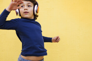 Tanzender kleiner Junge vor einer gelben Wand, der mit Kopfhörern Musik hört - VABF000148