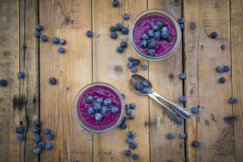 Zwei Gläser mit Chia-Blaubeer-Pudding und zwei Teelöffel auf Holz - LVF004517