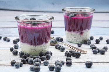 Zwei Gläser mit Chia-Blaubeer-Pudding, Blaubeeren und zwei Teelöffel auf Holz - LVF004520