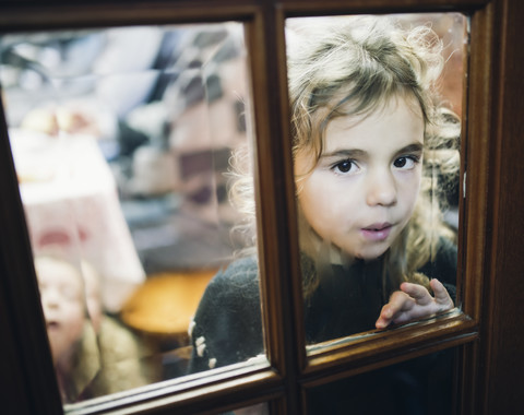Porträt eines kleinen Mädchens, das durch eine Glasscheibe einer Tür schaut, lizenzfreies Stockfoto
