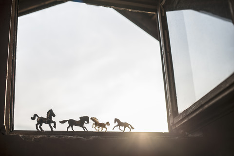 Silhouetten von vier Spielzeugpferden, die am geöffneten Fenster stehen, lizenzfreies Stockfoto
