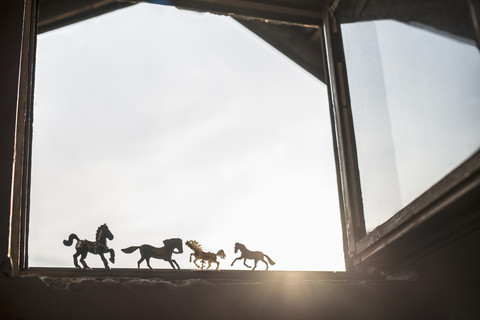 Silhouettes of four toy horses standing at opened window stock photo