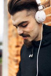 Porträt eines jungen Mannes, der mit Kopfhörern Musik hört - MGOF001432