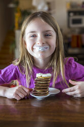 Porträt eines glücklichen Mädchens mit Schlagsahne auf den Lippen und einem Stapel von Mini-Pfannkuchen mit Schokolade - SARF002553