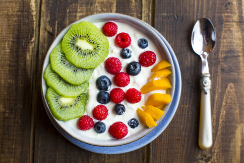 Bowl with yogurt and blueberries, kiwi, mango and raspberries, spoon on wood - SARF002560