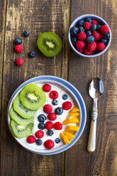 Bowl with yogurt and blueberries, kiwi, mango and raspberries, spoon on wood - SARF002561