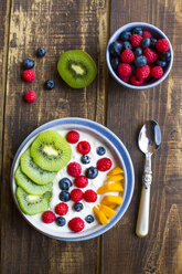 Schale mit Joghurt und Heidelbeeren, Kiwi, Mango und Himbeeren, Löffel auf Holz - SARF002561