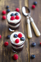 Joghurt mit roter Grütze, Heidelbeeren und Himbeeren in Gläsern auf Holz - SARF002563