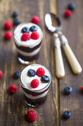 Yogurt with red fruit jelly, blueberries and raspberries in glasses on wood - SARF002563