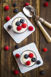 Joghurt mit roter Grütze, Heidelbeeren und Himbeeren in Gläsern auf Holz - SARF002564