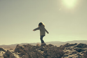 Spain, Consuegra, back view of little girl balancing on rocks in the mountains - ERLF000135