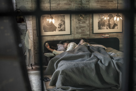Ein Mann liegt schlaflos im Bett und schaut auf den Wecker, während seine Frau neben ihm liegt, lizenzfreies Stockfoto