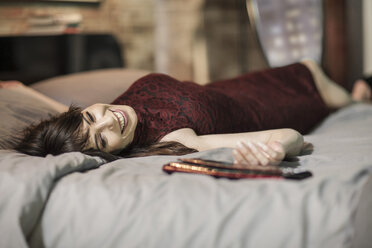 Smiling woman in evening dress on bed - ZEF008459