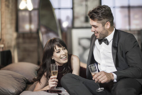 Lächelndes Paar in eleganter Kleidung trinkt Champagner im Bett - ZEF008461