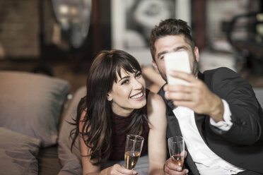 Lächelndes Paar in eleganter Kleidung trinkt Champagner im Bett und macht ein Selfie - ZEF008462