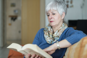 Eine Seniorin sitzt am Fenster auf der Couch und liest ein Buch. Available light. Grevenbroich, Nordrhein-Westfalen, Deutschland - FRF000382