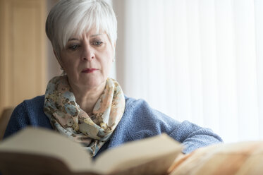 Portrait of senior woman sitting on the couch reading a book - FRF000383