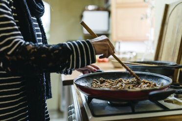 Woman cooking on gas stove in her kitchen, partial view - JRFF000425