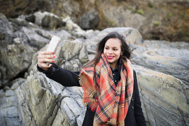 Spanien, Ferrol, Porträt einer lächelnden Frau, die ein Selfie mit ihrem Smartphone vor einem Felsen macht - RAEF000879