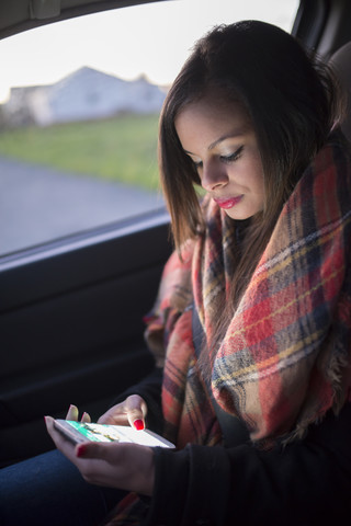 Spanien, Ferrol, Porträt einer jungen Frau, die in einem Auto sitzt und auf ihr Smartphone schaut, lizenzfreies Stockfoto