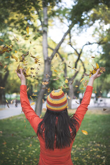 Rückenansicht einer Frau mit Wollmütze, die Herbstblätter in die Luft wirft - DEGF000639