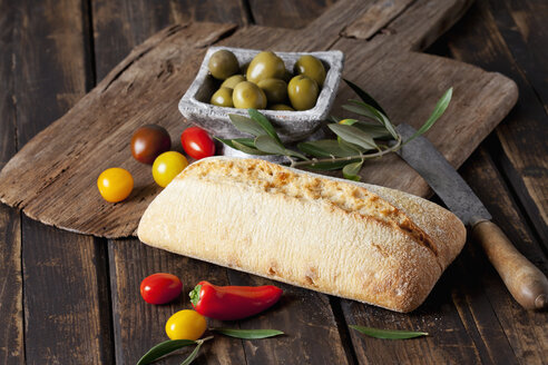 Ciabatta-Brot mit grünen Oliven in Schale, Tomaten und Mini-Paprika auf Holz - CSF027163