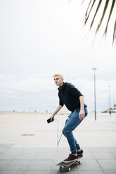 Spanien, Torredembarra, junger Mann mit Smartphone auf seinem Skateboard stehend - JRFF000447