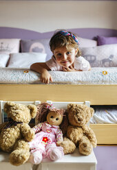 Porträt eines kleinen Mädchens auf dem Bett liegend mit Spielzeug im Vordergrund - MGOF001437