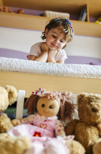 Porträt eines kleinen Mädchens, das auf dem Bett liegt und seine Spielsachen im Vordergrund betrachtet - MGOF001438