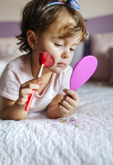 Porträt eines kleinen Mädchens auf dem Bett liegend mit Handspiegel und Schönheitspinsel - MGOF001439
