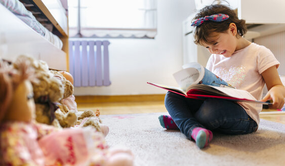 Laughing little girl sitting on the floor watching picture book - MGOF001441