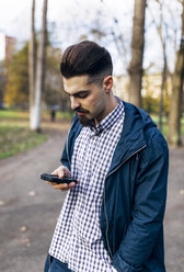 Junger Mann schaut im Park auf sein Smartphone - MGOF001450