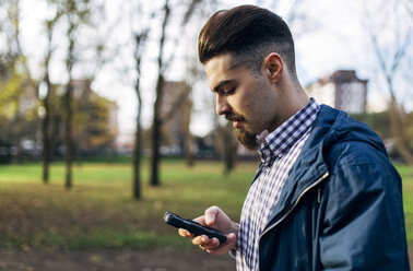 Junger Mann schaut im Park auf sein Smartphone - MGOF001452