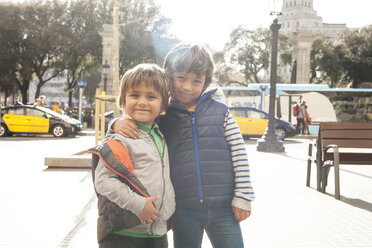 Spain, Barcelona, portrait of two little brothers standing arm in arm at backlight - VABF000165