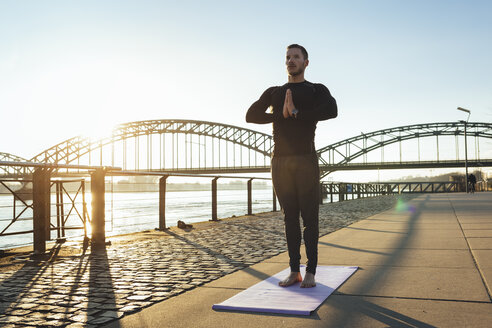 Deutschland, Köln, Junger Mann übt Yoga am Flussufer - MADF000810