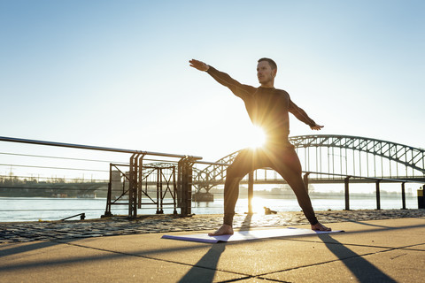 Deutschland, Köln, Junger Mann übt Yoga am Flussufer, lizenzfreies Stockfoto