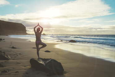 Spain, Fuerteventura, El Cotillo, back view of woman practicing yoga on the beach at sunset - GEMF000734