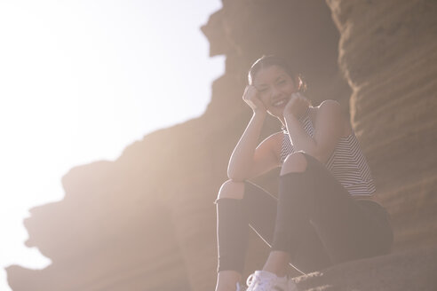 Spanien, Teneriffa, junge Frau sitzt vor einer Felswand im Gegenlicht - SIPF000190