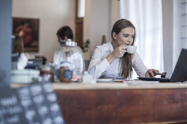 Young woman sitting at coffee bar working and drinking coffee - ZEF008516