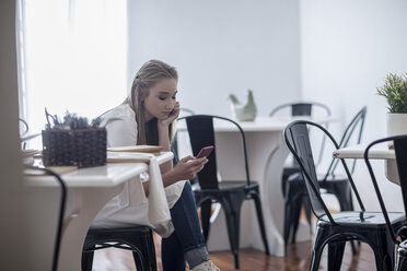 Young waitress sitting restaurant looking at smart phone - ZEF008530