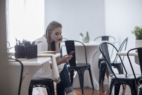 Junge Kellnerin sitzt im Restaurant und schaut auf ihr Smartphone - ZEF008530