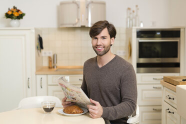 Porträt eines lächelnden Mannes, der mit einer Zeitung am Frühstückstisch sitzt - SHKF000494
