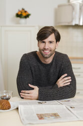 Porträt eines lächelnden Mannes, der mit einer Zeitung am Frühstückstisch sitzt - SHKF000496