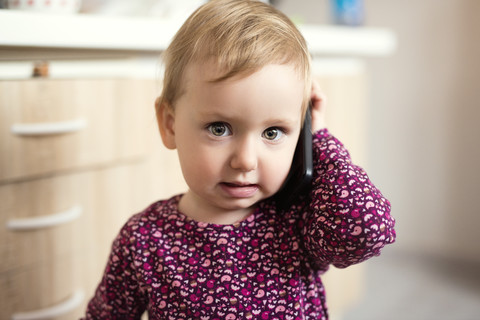 Porträt eines blonden Kleinkindes, das mit einem Smartphone spielt, lizenzfreies Stockfoto