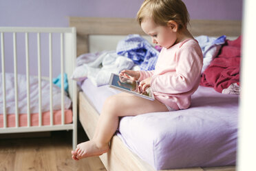 Kleinkind auf dem Bett sitzend und mit digitalem Tablet spielend - HAPF000240