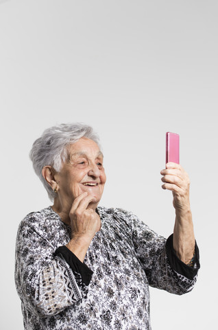 Porträt einer lächelnden älteren Frau, die ein Selfie mit einem Smartphone vor einem weißen Hintergrund macht, lizenzfreies Stockfoto