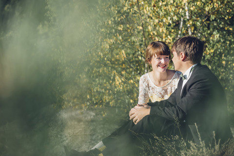 Glückliches Brautpaar sitzt von Angesicht zu Angesicht in der Natur, lizenzfreies Stockfoto