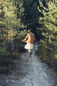 Rückenansicht einer altmodisch gestylten Frau mit Windlicht, die auf einem Weg geht - MJF001724