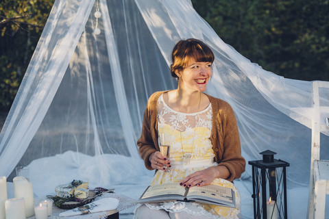 Porträt einer lachenden Frau mit Buch und Glas Champagner in einem romantischen Lager in der Natur, lizenzfreies Stockfoto